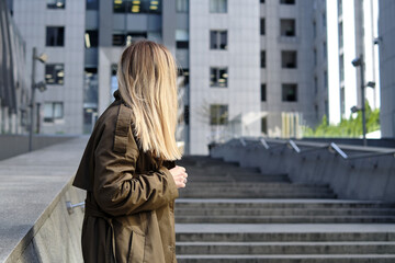 Woman stands against a business center. Young businessperson near an office building in the financial district of the city. Urban concept. Walk in a modern city