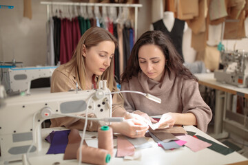 Two female fashion designers were looking at samples of sketches in a sewing workshop