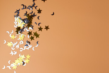 On a peach background, shiny confetti in the shape of the moon and stars. Copy space.