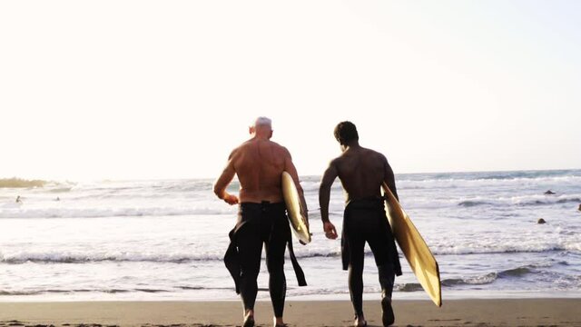 Multi generational surfer men walking to the beach with body boards - Multiracial people, lifestyle and sport concept