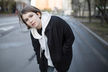 Fototapeta premium A serious short-haired girl in a white hoodie with a hood, a black raincoat and jeans walks down the street.