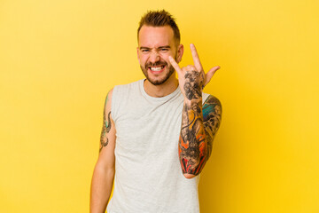 Young tattooed caucasian man isolated on yellow background showing rock gesture with fingers