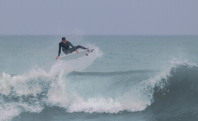 Surfer doing an aerial on a cloudy day with a nice bluish wave