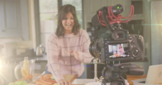 Animation of glowing light over camera with female vlogger recording culinary vlog at home