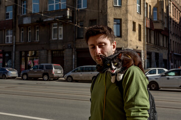 A man promenades with his cat sits on his shoulder and mews.
