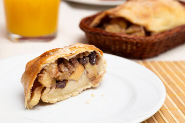 Sweet strudel on a white plate on a table with glass of orange juice.