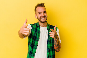 Young tattooed caucasian man isolated on yellow background pointing to front with fingers.