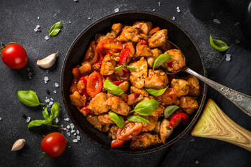 Chicken meat with vegetables in tomato sauce on black.