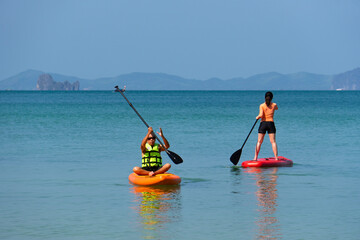 asian senior father playing standing up paddleboard or SUP with young daughter at blue sea on summer vacation. family together concept