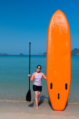 young sporty asian woman standing at beach while holding stand-up paddle board preparing to play blue sea in sunny day of summer vacation