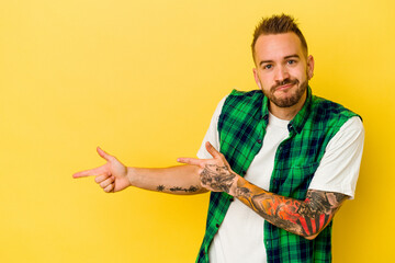 Young tattooed caucasian man isolated on yellow background pointing with forefingers to a copy space, expressing excitement and desire.