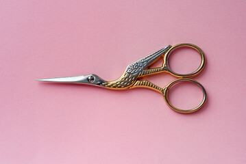 Scissors in the form of a bird made of gold and silver on a pink background.