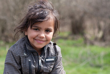 A portrait of smiling beautiful little gypsy girl in a Roma settlement - obrazy, fototapety, plakaty
