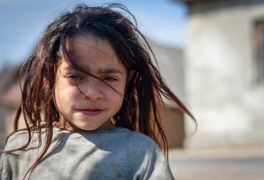 A portrait of a beautiful little roma girl with unwashed hair on blurred background in a Roma settlement