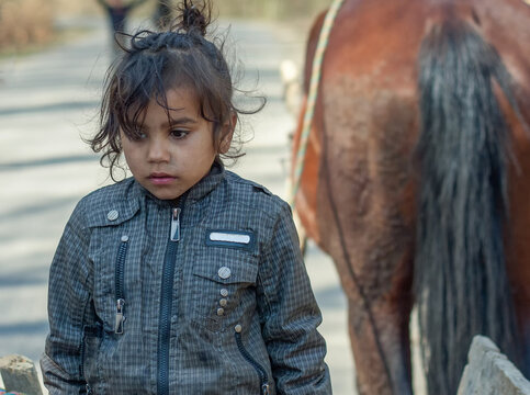 Beautiful sad little gypsy girl in a Roma settlement on blurred background of a horse 