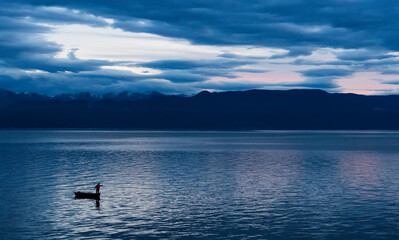 Beautiful sunset on the sea or lake with fish boat and mysterious reflactions on the surface of water.