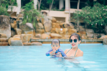 Asian mother and little son enjoying swimming in a swimming pool in summer vacation.