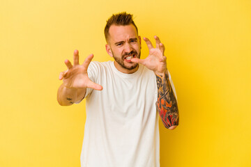 Young tattooed caucasian man isolated on yellow background upset screaming with tense hands.