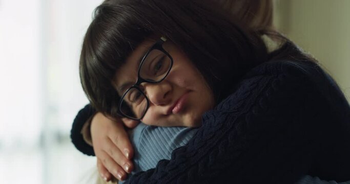 Authentic shot of happy young woman embracing with affection teen sister with down syndrome at home. Concept of love, family, trust, protection, handicapped, healthcare, disability, love, friendship