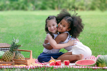 Two child girl of different ethnicities hugging each other on a picnic cloth at the park,  friendship between different races and religions