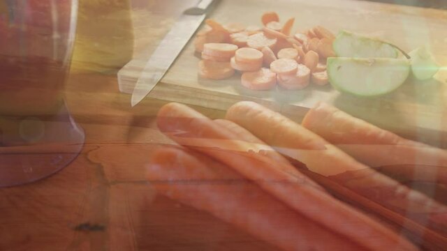 Animation of flickering spots of light over cut carrot, knife and chopping board in kitchen
