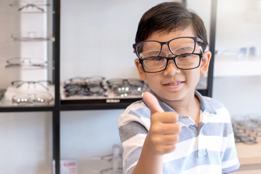 Asian children have fun choosing and trying on eyeglasses in an eyeglass shop, make a joke by wearing 2 glasses on your face, looking at camera