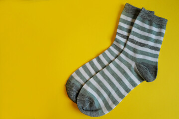 two gray with white stripes socks lie on a yellow background top view