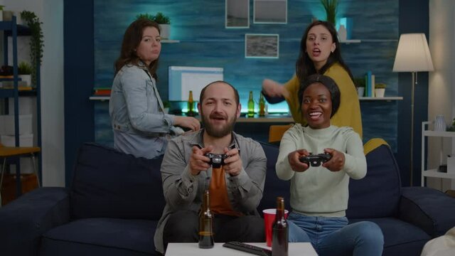 Woman with blak skin playing online videogames against man friends during competition simulation using controller. Group of mixed race winning game while sitting on sofa in living room late at night