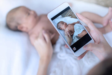 Mother taking a photo of her newborn baby by smartphone, selective focus - obrazy, fototapety, plakaty