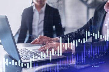 Two traders man and woman researching historic data to predict stock market behavior using laptop. Internet trading concept. Forex and financial hologram chart. Forecasting and planning.