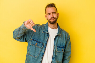 Young tattooed caucasian man isolated on yellow background showing a dislike gesture, thumbs down. Disagreement concept.