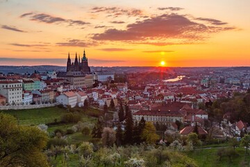 Fototapeta na wymiar Prague, Czech Republic - May 3 2021: Colorful sunrise view of the city from Petrin hill with the castle, garden, trees, river and buildings. Clouds on the yellow, orange, pink and blue sky.