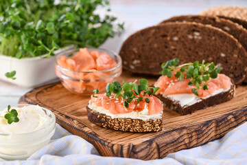 Open sandwich with cheese cream on a slice of rye bread with cereals, slices of marinated salmon, and radish sprouts.