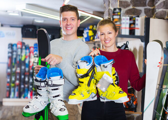 Happy young customers are demonstrating their choice of ski and boots for skiing in sport shop.