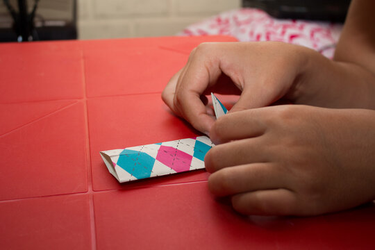 a woman's hands making an origami figure on a red table