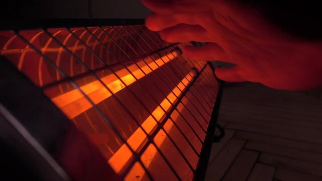 A man warms his hands over an infrared heater in a room in cold weather. Close-up