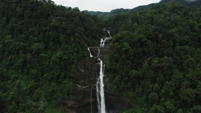 Stunning white water falls from steep rocky cliff in tropical jungle, aerial