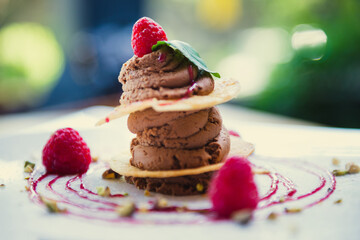 Chocolate mousse dessert with puff pastry and raspberries in restaurant on sunny day, blur background.
