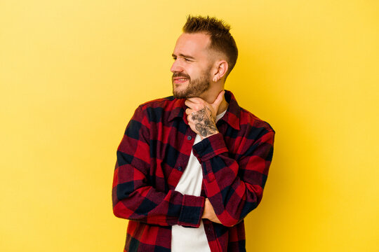 Young tattooed caucasian man isolated on yellow background suffers pain in throat due a virus or infection.