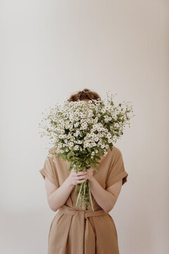 Woman hiding behind a bunch of daisies on white background.