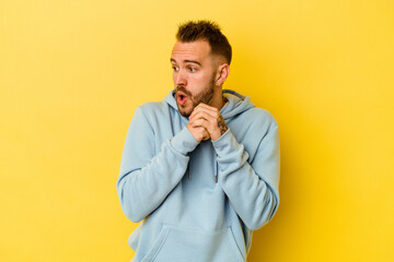 Young tattooed caucasian man isolated on yellow background praying for luck, amazed and opening mouth looking to front.