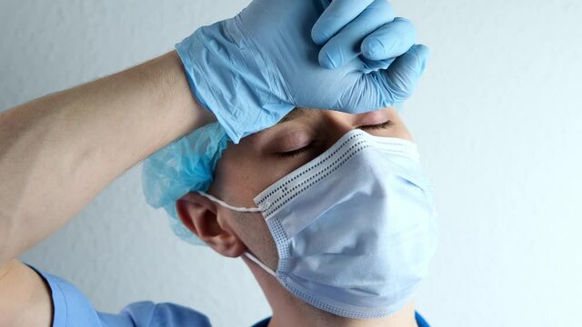 close-up of face young doctor in white mask, under the pressure of problems wearily closes his eyes, concept COVID-19 coronavirus, of psychological stress, condemnation