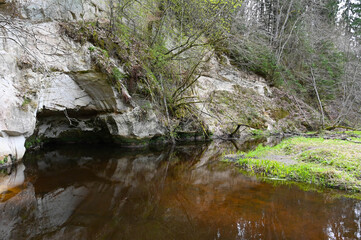 Rock outcrop with a cave in the forest, which is reflected in the forest river in spring.