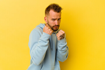 Young tattooed caucasian man isolated on yellow background throwing a punch, anger, fighting due to an argument, boxing.