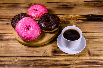 Cutting board with glazed donuts and cup of coffee on a wooden table