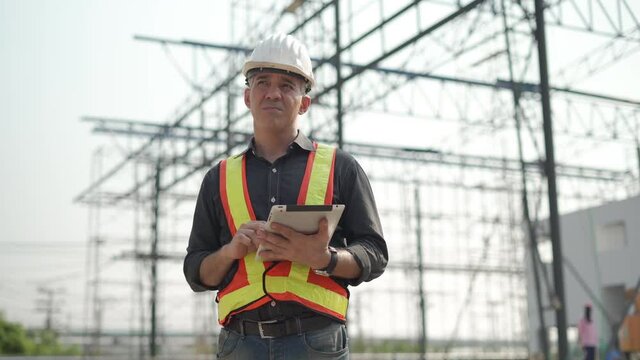 senior construction worker or architect using digital tablet checking structure in construction site outdoors with Hot weather and sunny . builders in hard hat inspecting and working in workplace