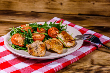 Roasted chicken breasts and salad with arugula and cherry tomatoes in a ceramic plate