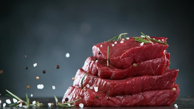 Flying pieces of raw beef steaks falling on table with spice. Filmed on high speed cinema camera, 1000 fps.