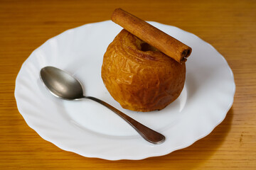 Tasty Baked Apple decorated with a cinnamon stick and a metal spoon on a plate and wooden background