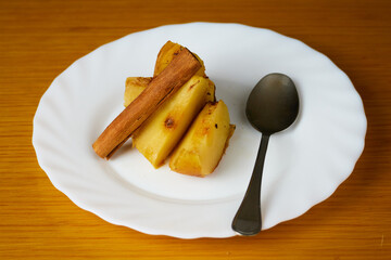 Tasty Baked Apple slices decorated with a cinnamon stick and a metal spoon on a plate and wooden background